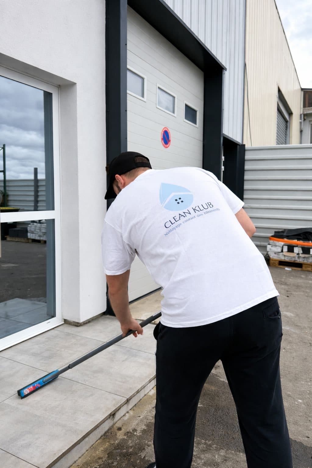 Agent CLEAN KLUB en tenue nettoyant l'entrée d'un bâtiment professionnel